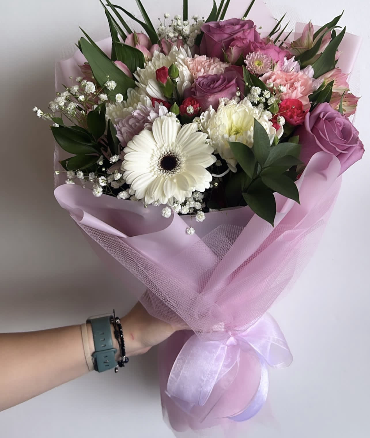 Handheld bouquet of pink, purple, and white flowers wrapped in pink paper