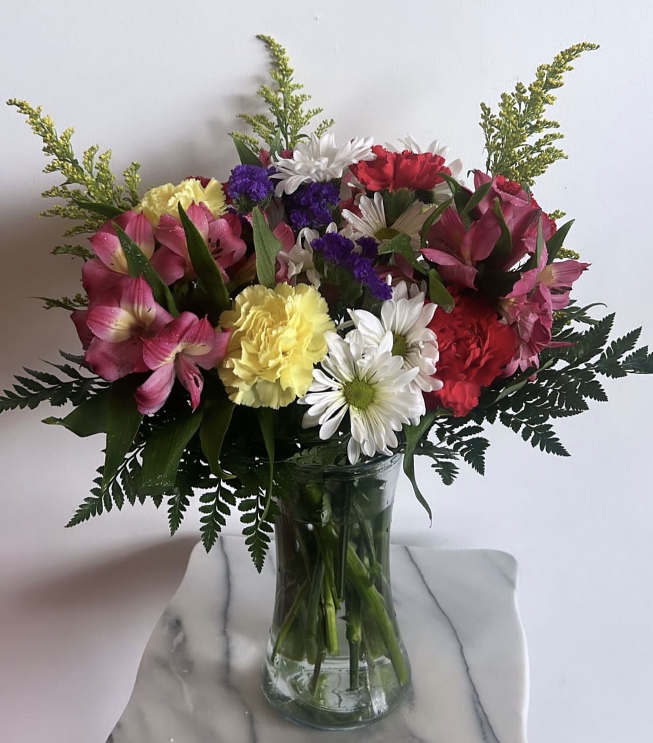 Mixed bouquet of pink, white, yellow, and purple flowers in a glass vase