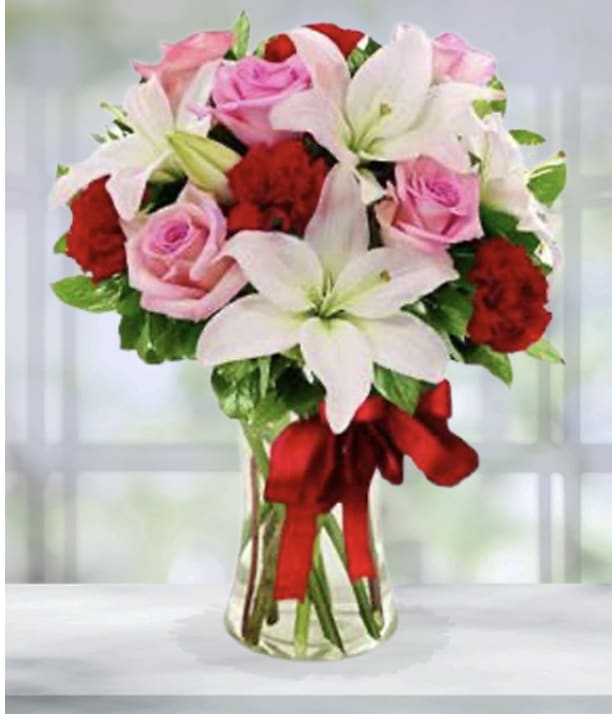 Pink roses and white lilies in a clear glass vase with a red ribbon