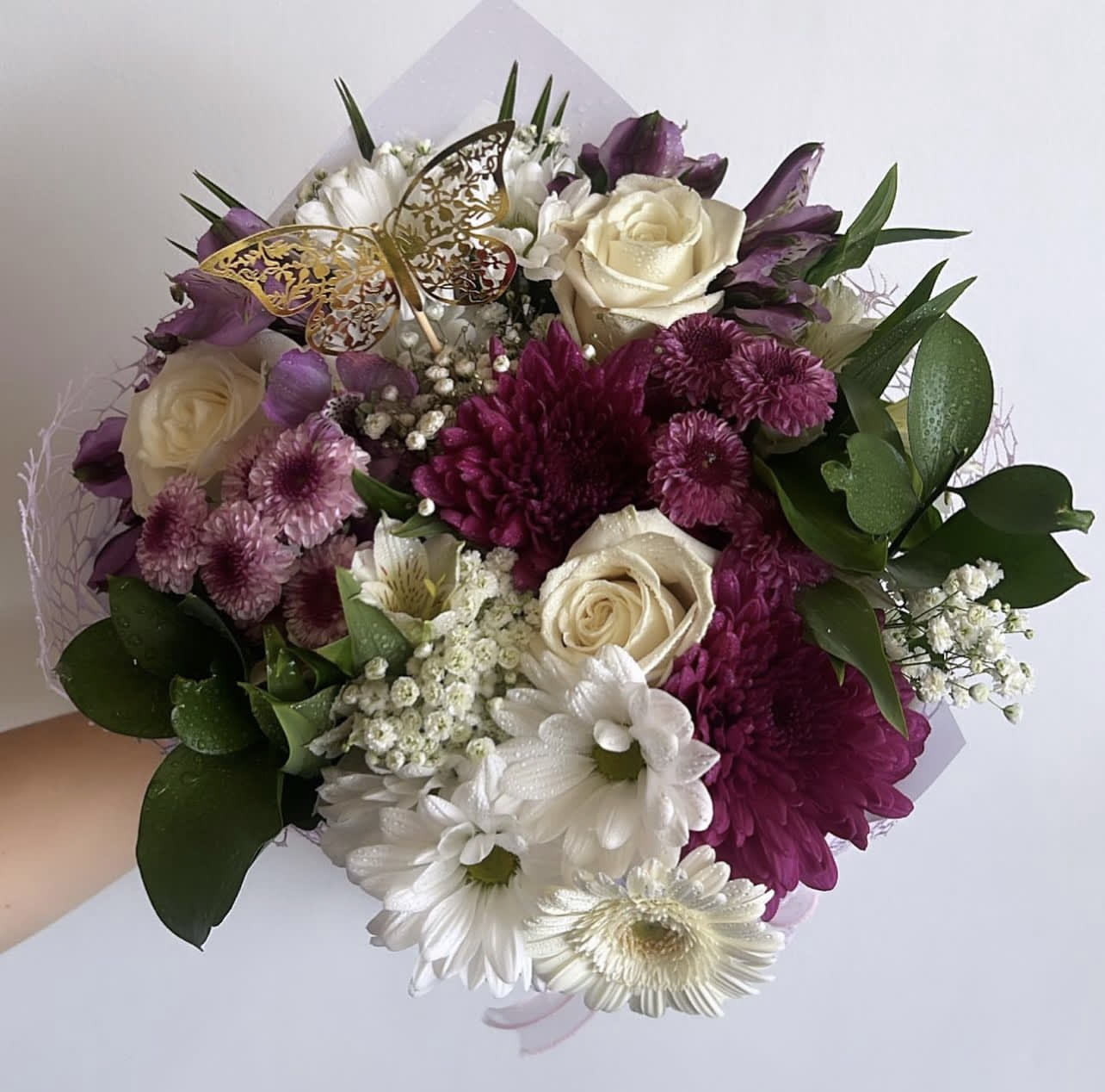 Handheld bouquet of white, purple, and pink flowers with a butterfly pick