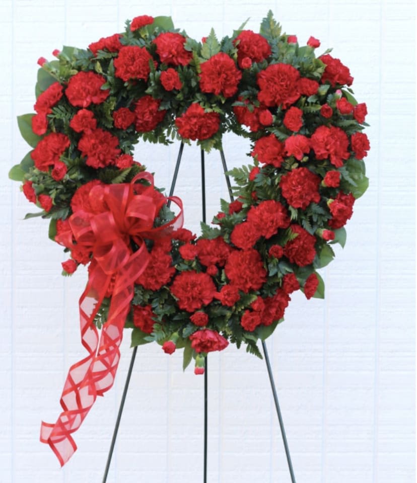 Heart-shaped wreath of red carnations on a stand with a red ribbon bow