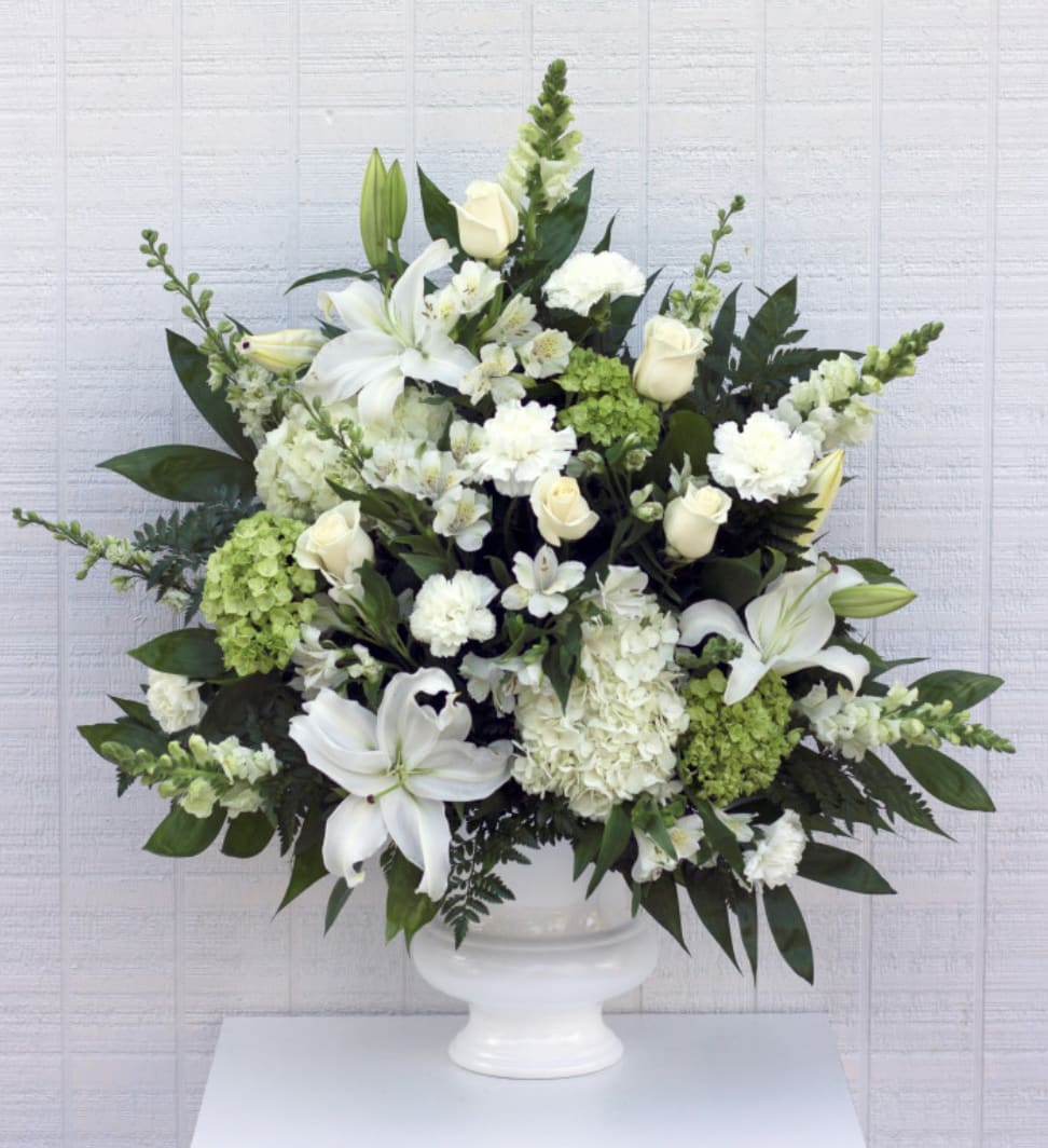 White lilies and roses arranged in a white pedestal vase