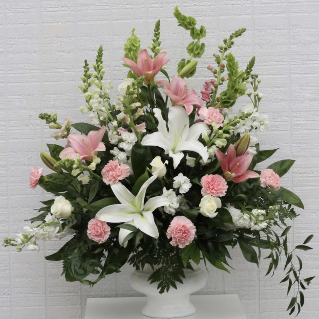 Pink and white lily arrangement in a white pedestal vase