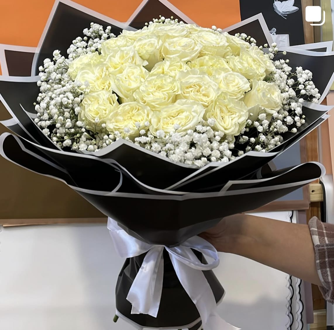 Bouquet of pale yellow roses wrapped in black paper with white baby's breath