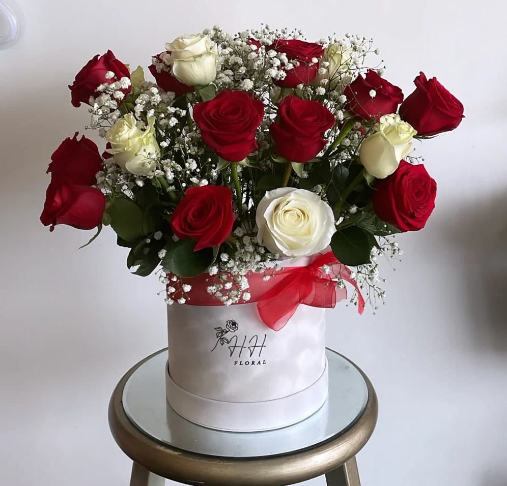 Red and white roses arranged in a white hat box with a red ribbon