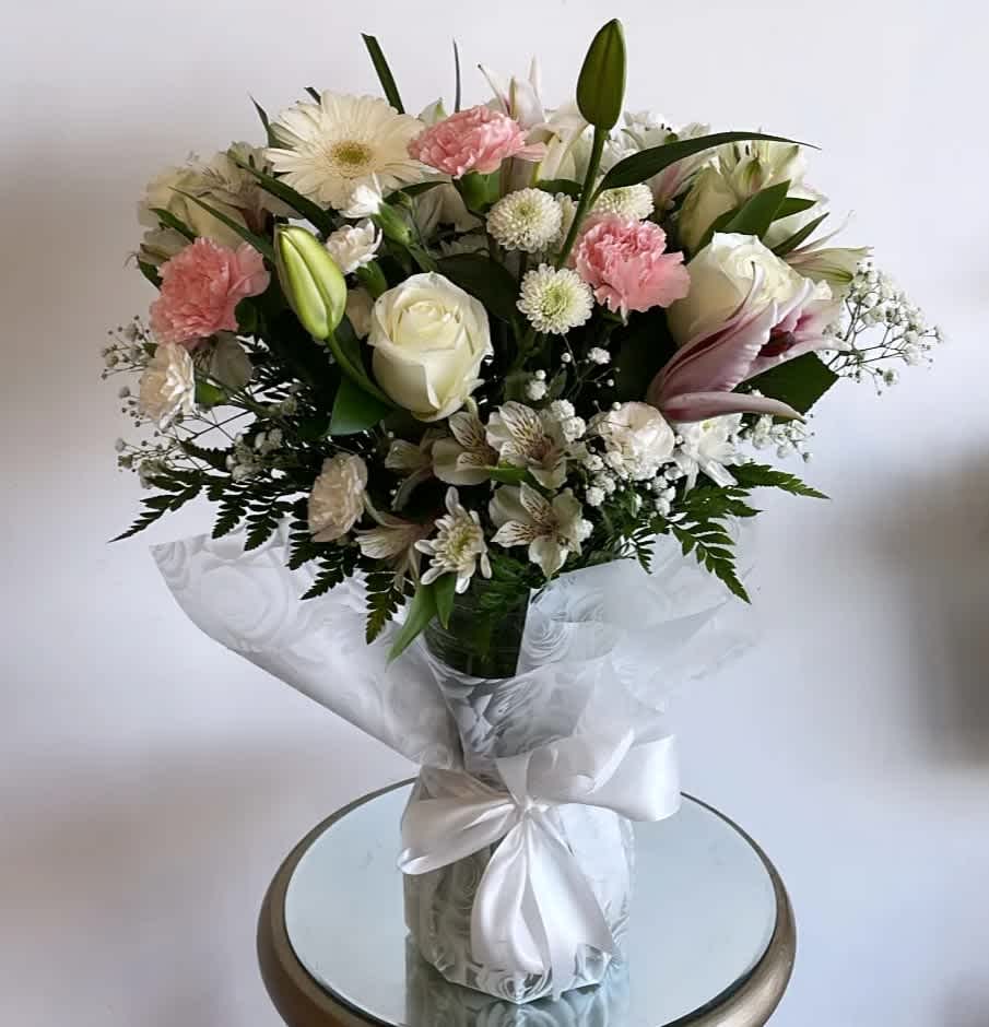Bouquet of white and pink flowers in a clear glass vase with a white ribbon