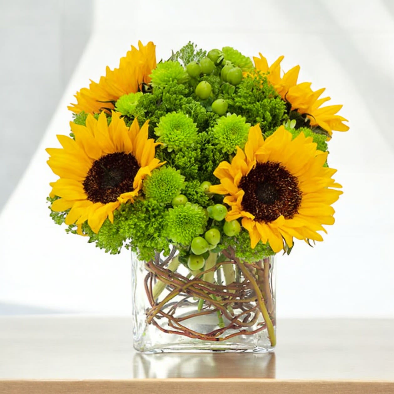 Sunflowers and green pom flowers arranged in a clear square vase