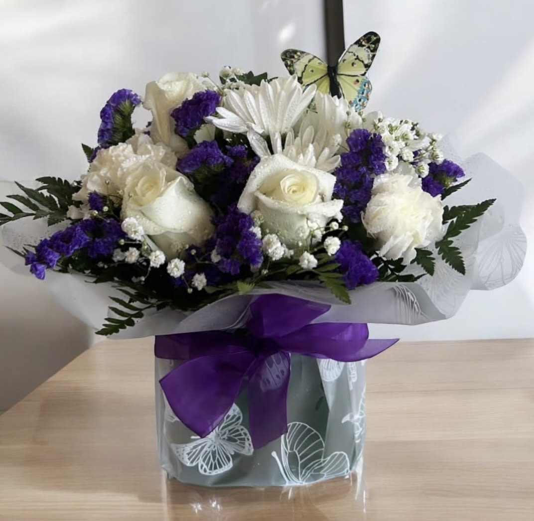 White roses and purple flowers in a wrapped bouquet with a purple ribbon