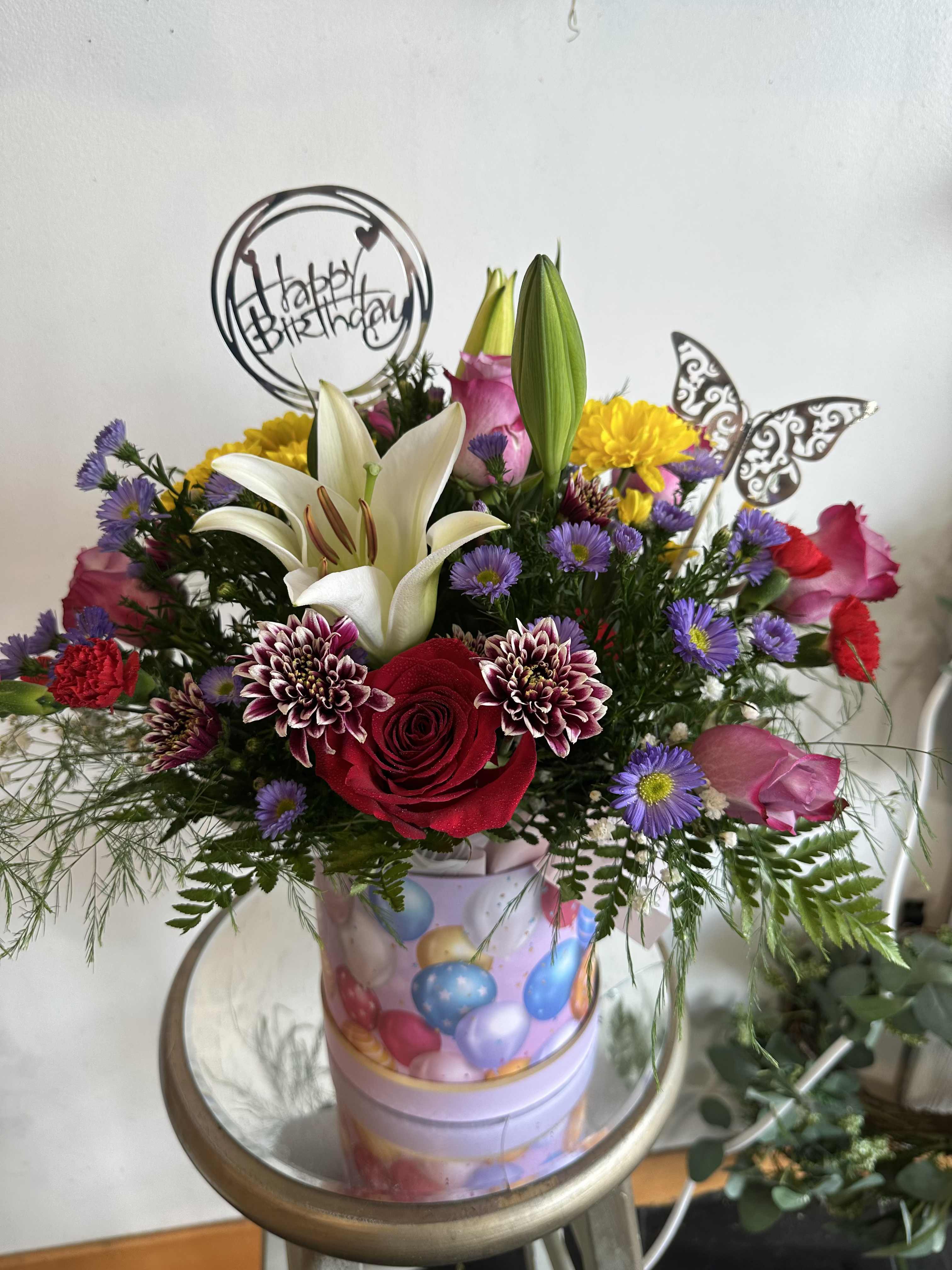 Mixed bouquet with roses, lilies, and daisies in a birthday container
