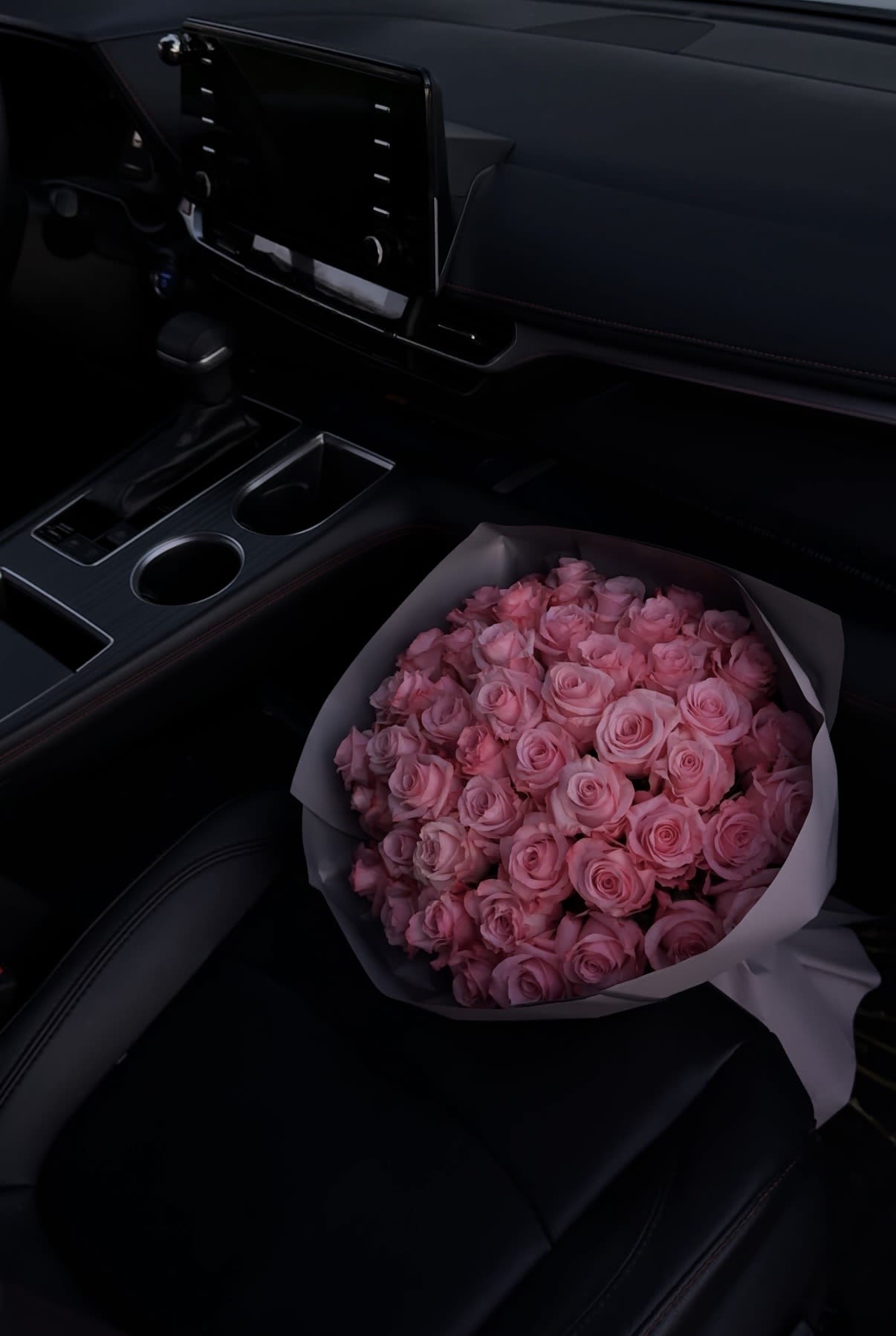 Bouquet of pink roses wrapped in white paper on a car seat