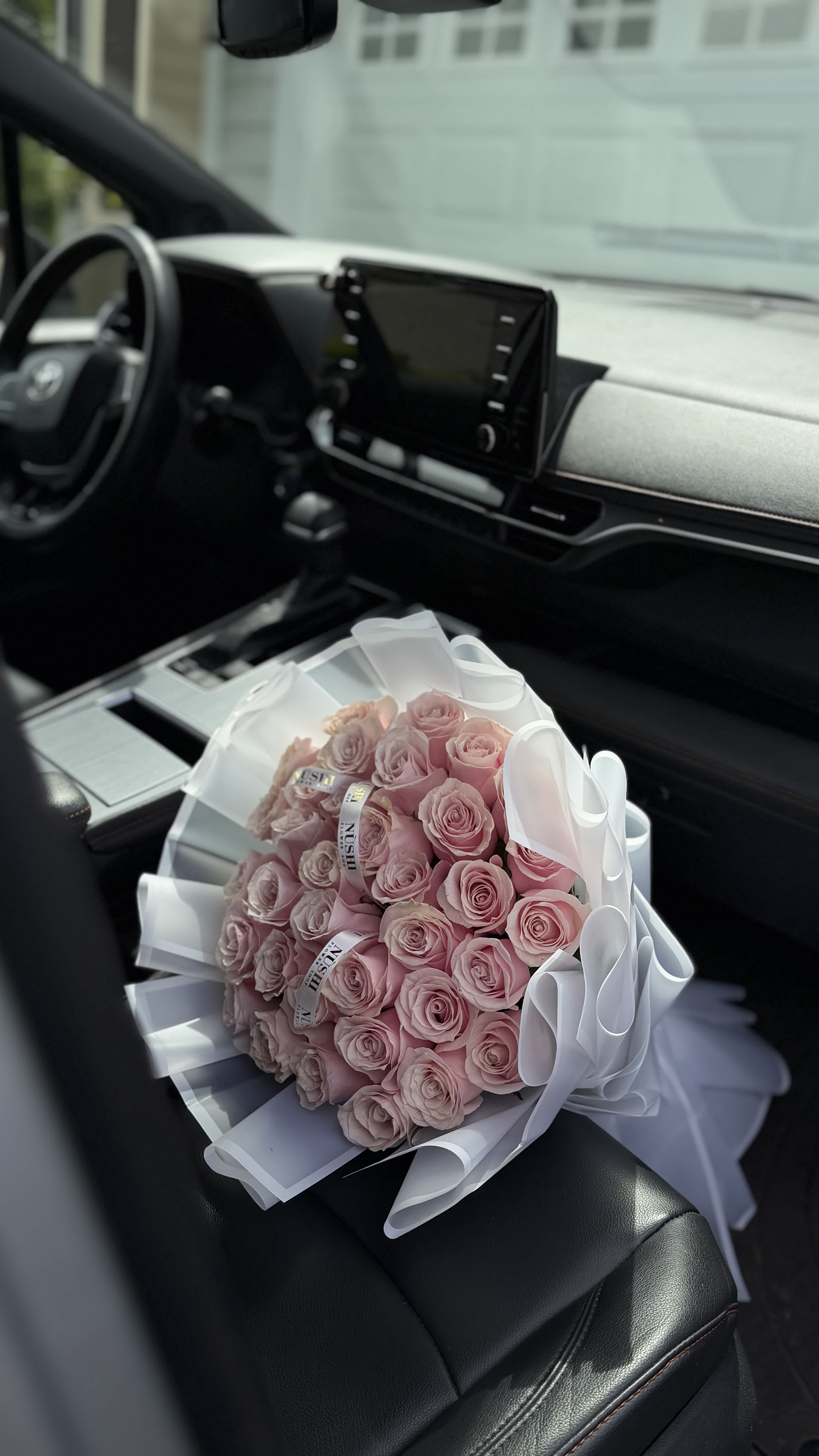 Bouquet of pale pink roses wrapped in white paper and ribbon on a car seat
