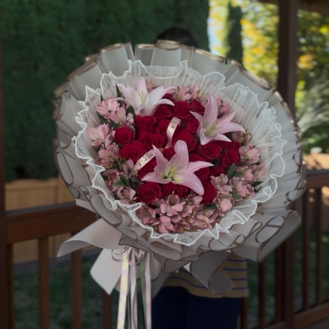 Bouquet of red roses and pink lilies wrapped in white paper