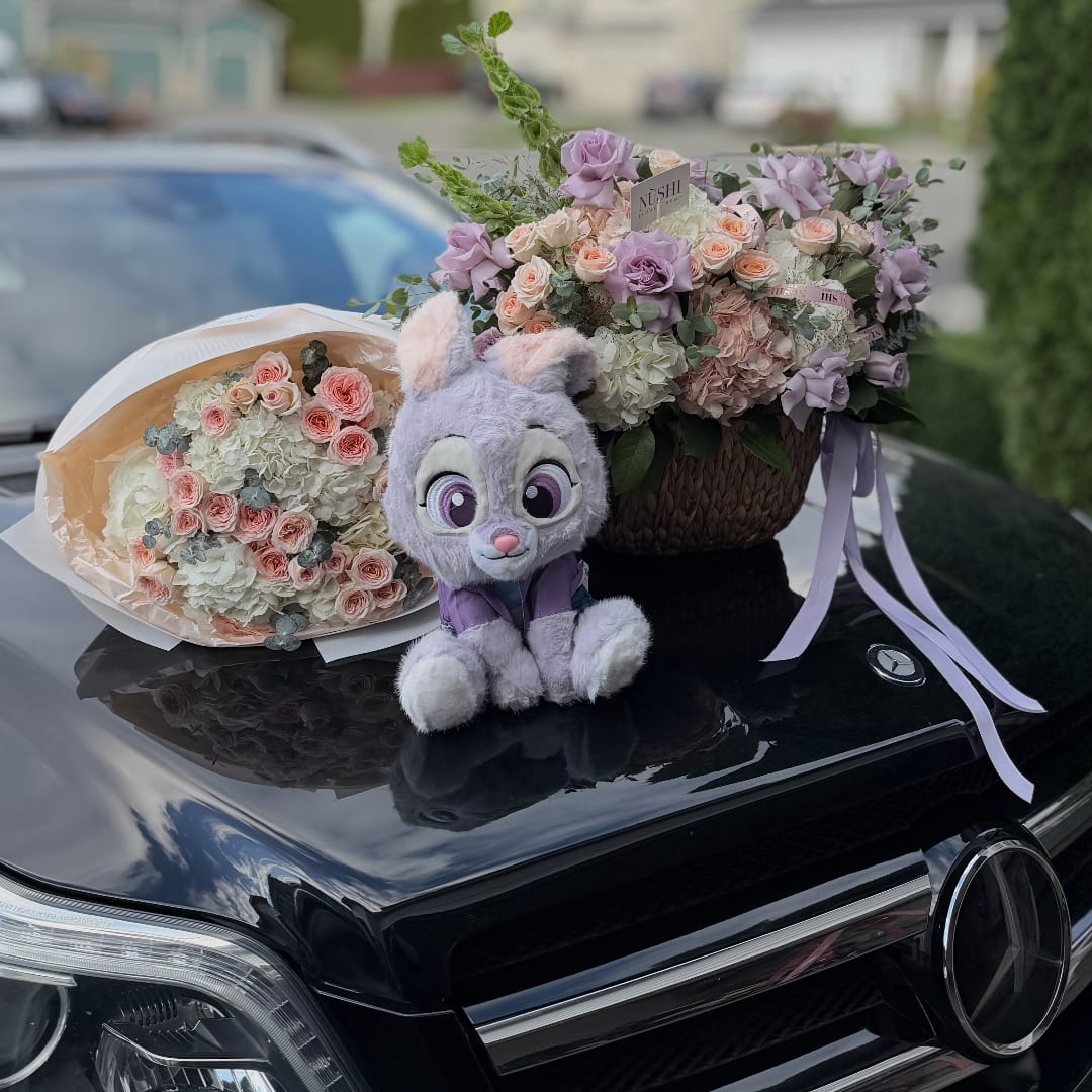 Two pastel flower arrangements with a plush bunny on a car hood