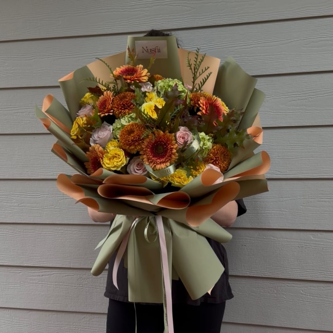 Large bouquet of orange, yellow, pink, and green flowers wrapped in paper