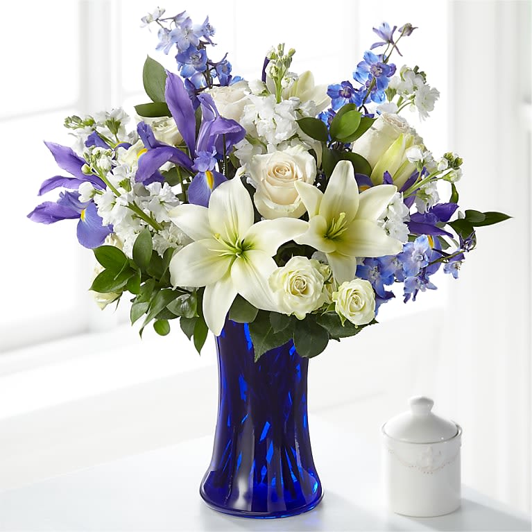 White lilies, roses, and blue-purple flowers in a cobalt vase