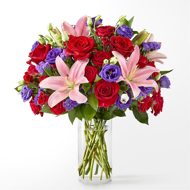 Bouquet of red roses, pink lilies, and purple blooms in a clear glass vase