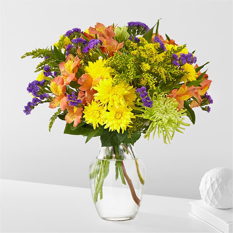 Mixed bouquet of yellow, purple, and peach flowers in a clear glass vase