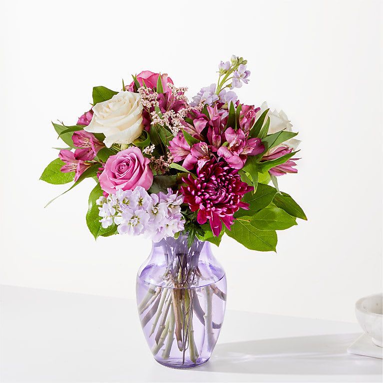 Pink and white mixed flower bouquet in a purple glass vase