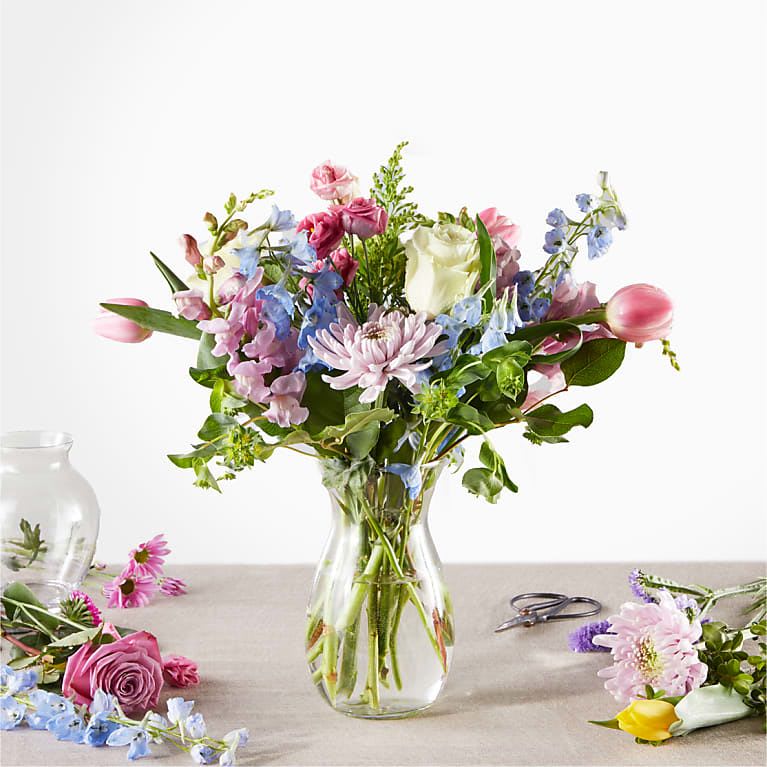 Mixed bouquet of pink, blue, and white flowers in a clear glass vase