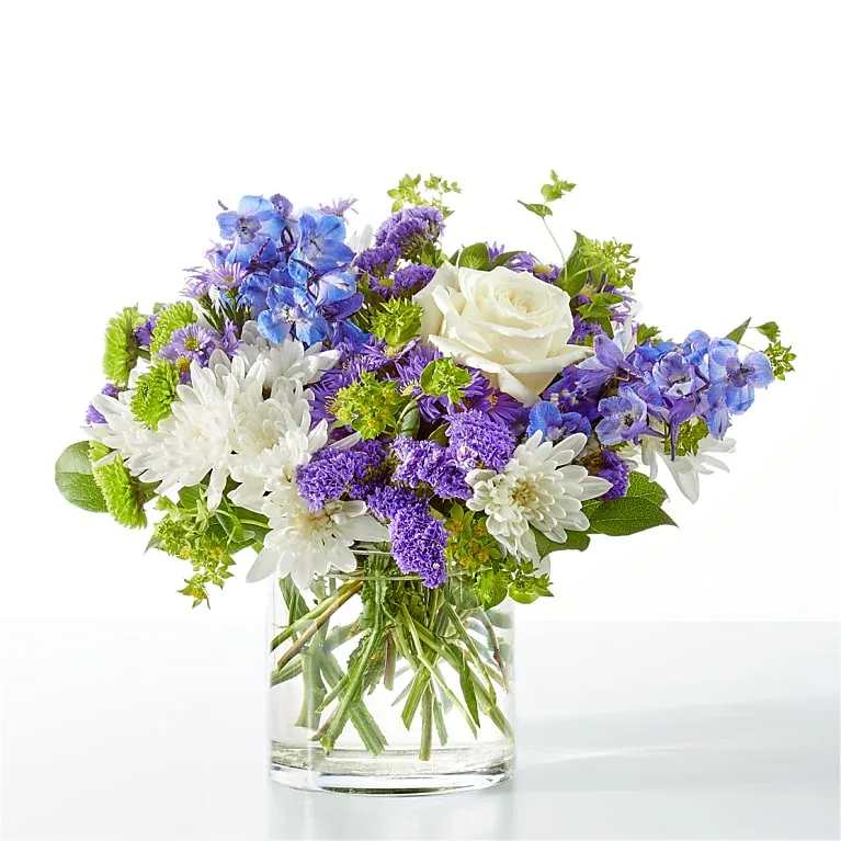 Blue, purple, and white flowers arranged in a clear glass vase
