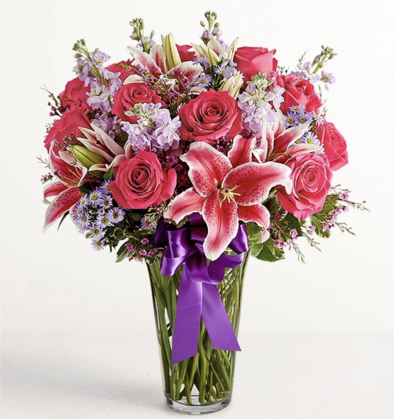 Pink roses and lilies in a clear glass vase with a purple ribbon