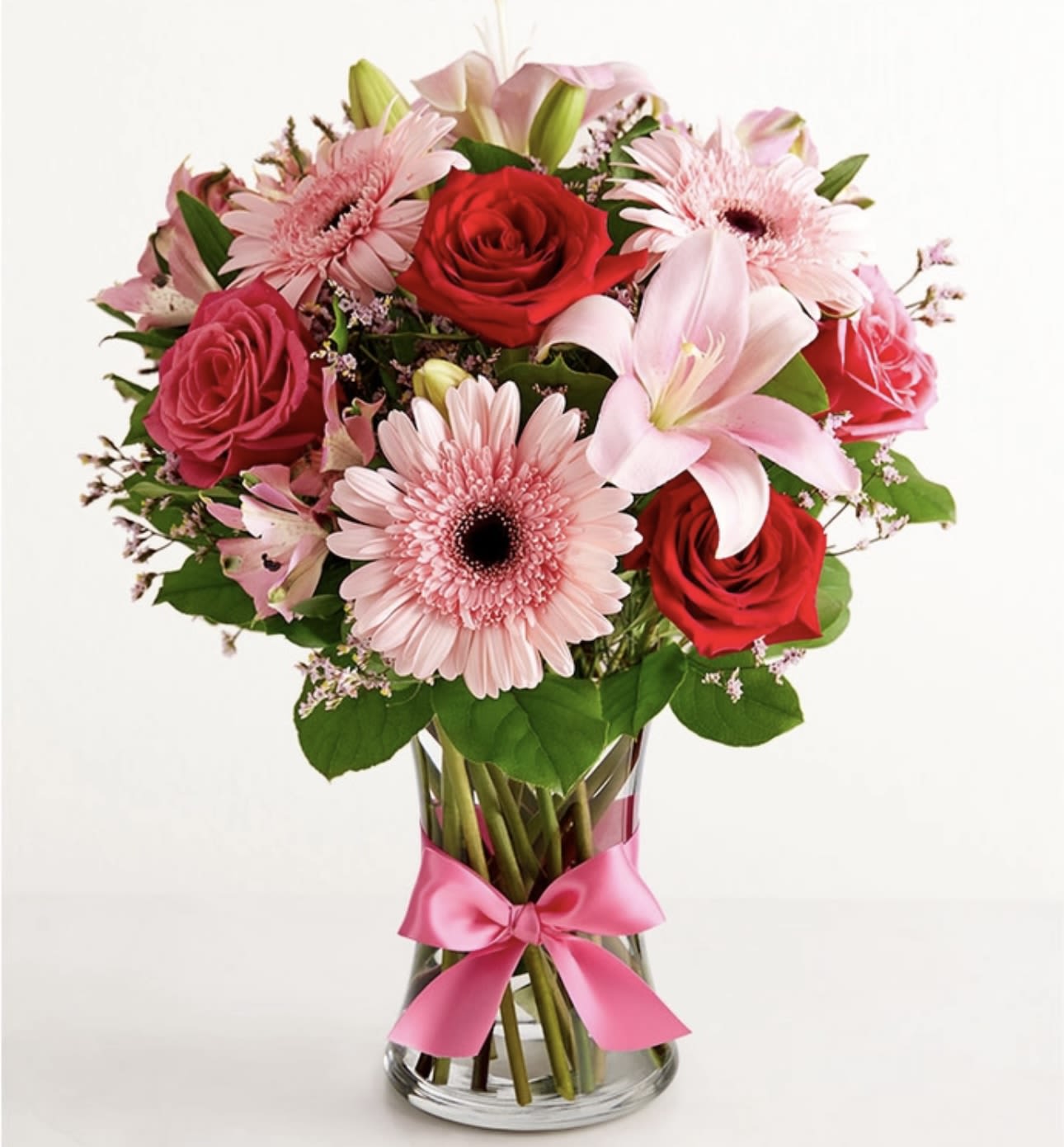 Pink and red flower bouquet in a glass vase with a pink ribbon