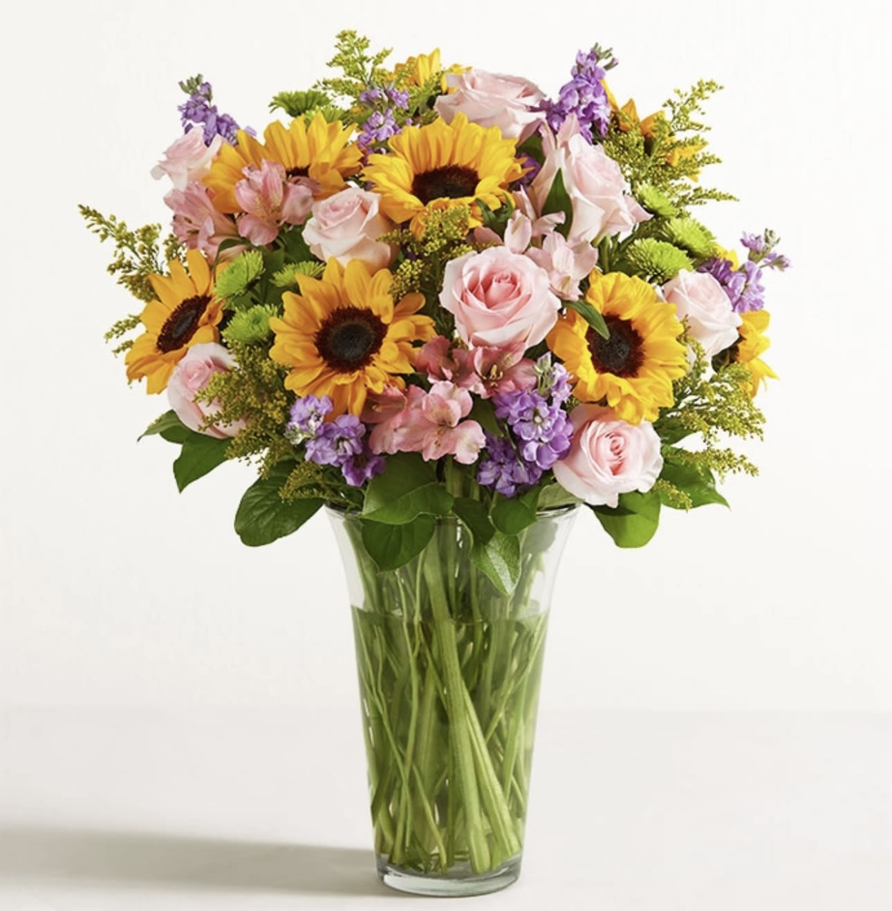Bouquet of sunflowers, pink roses, and purple flowers in a glass vase