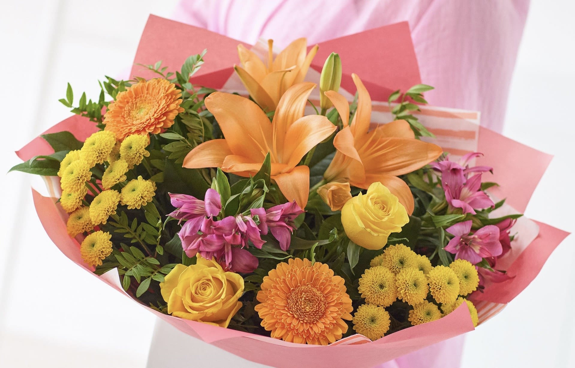 Bouquet of orange lilies, yellow roses, and pink alstroemeria in pink wrap