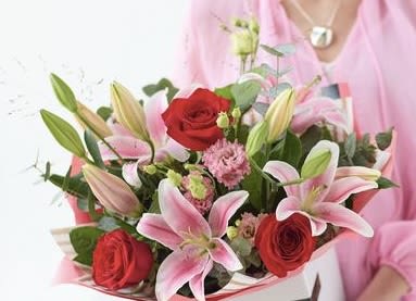 Bouquet of pink lilies and red roses held by a person in pink