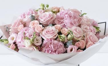 Bouquet of pale pink roses and ruffled pink flowers wrapped in white paper