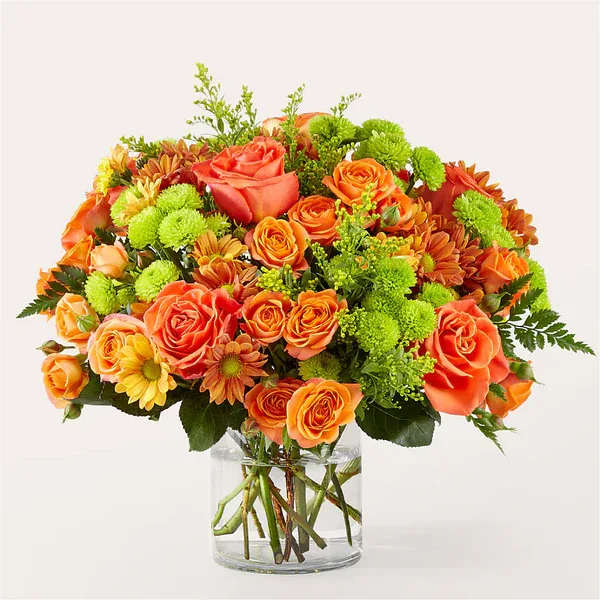 Orange roses and green mums arranged in a clear glass vase
