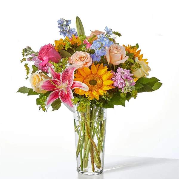 Mixed bouquet with roses, lilies, and a sunflower in a clear glass vase