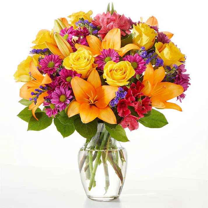 Mixed bouquet of yellow roses, orange lilies, and purple daisies in a glass vase