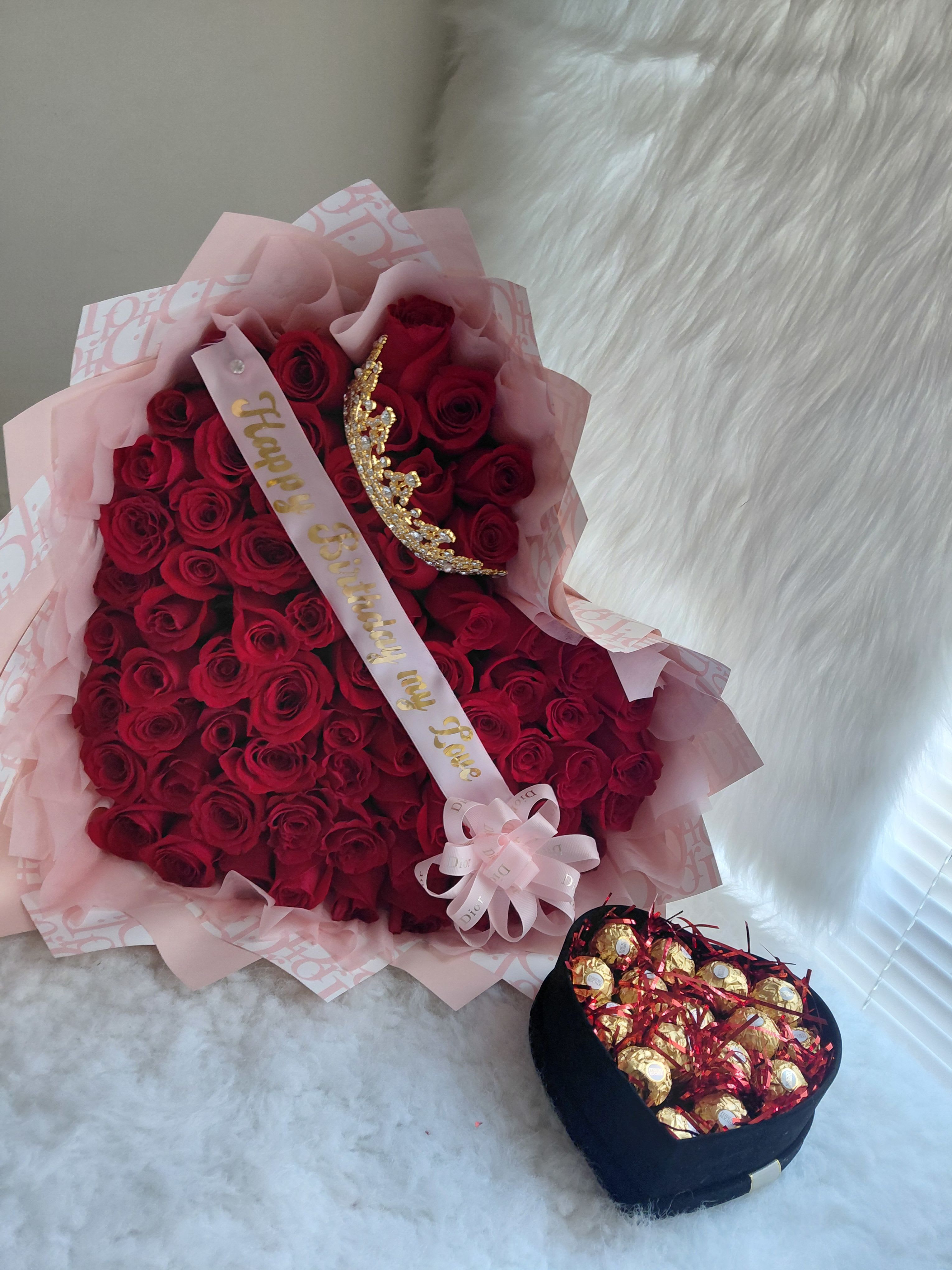 Bouquet of red roses with a birthday ribbon and tiara, plus a box of chocolates.