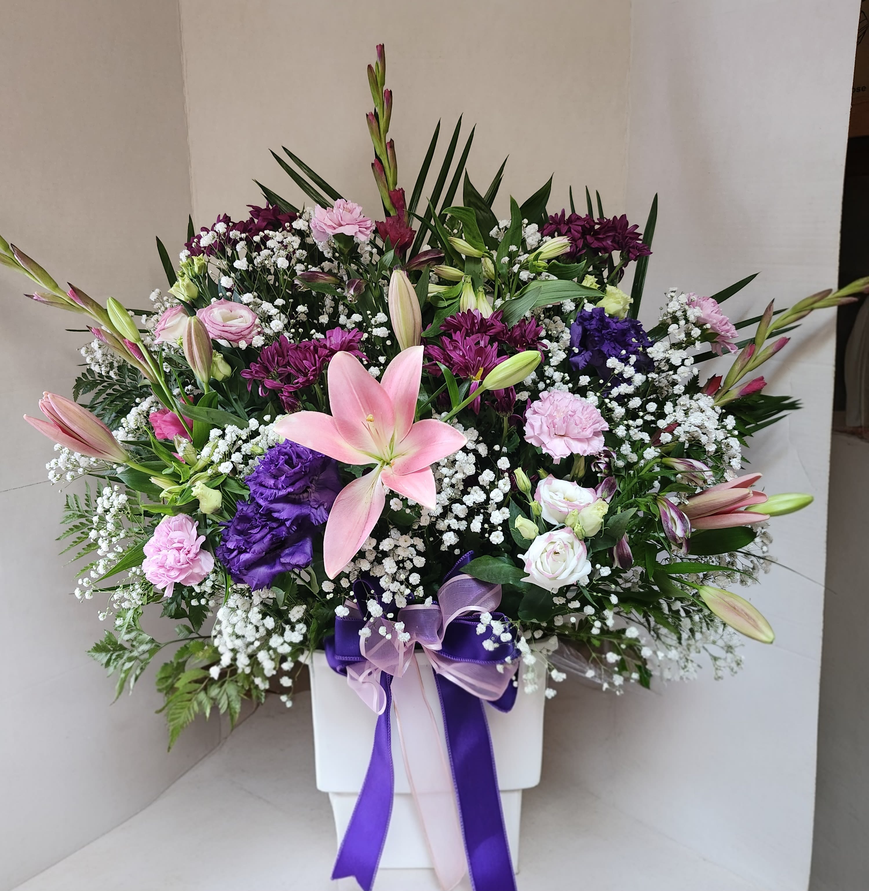 Pink lilies and mixed purple flowers in a white vase with ribbon