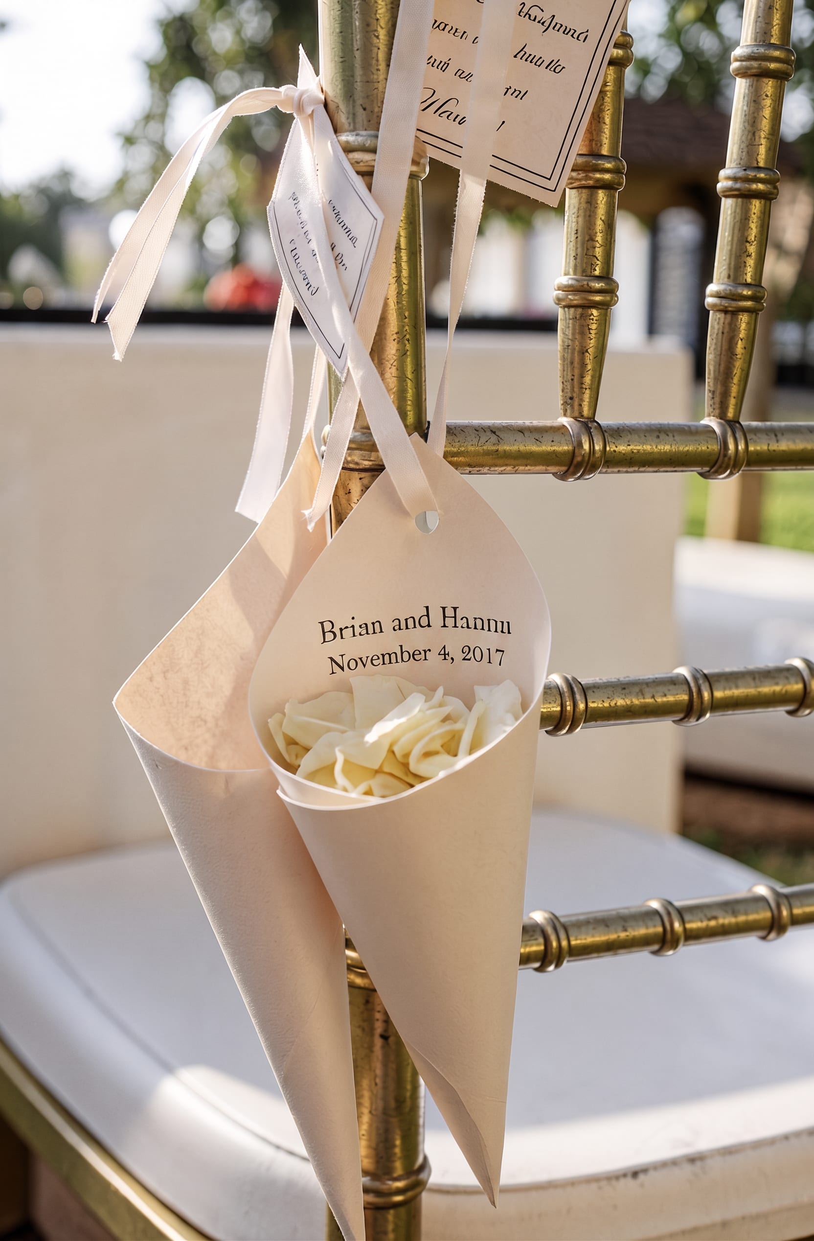 Cream rose petals in paper cones tied to a gold chair