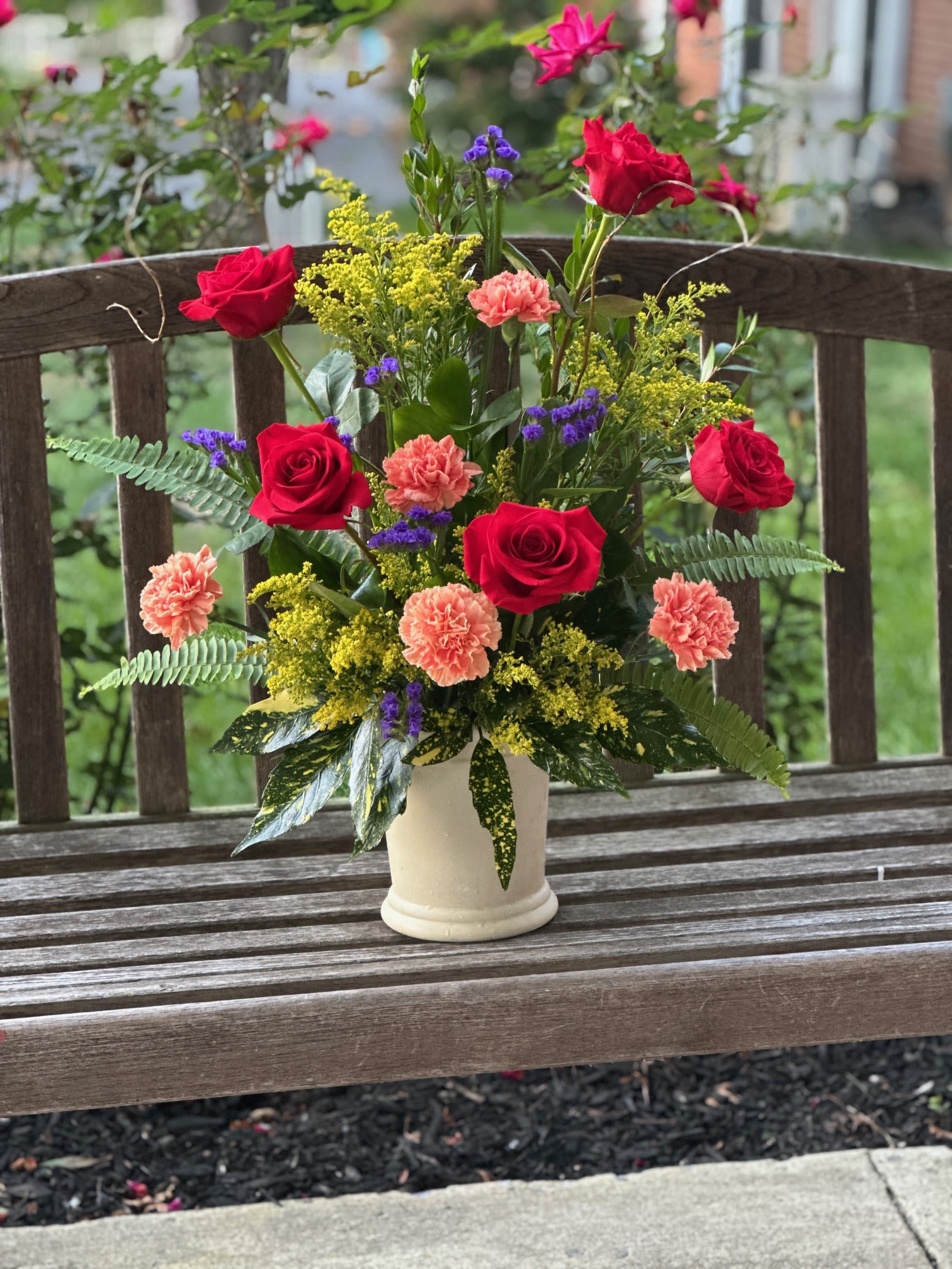 Mixed bouquet of red roses, peach carnations, and purple filler in a white vase