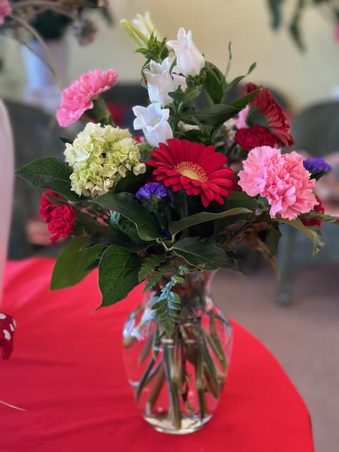Mixed bouquet of gerbera daisies, carnations, hydrangea, and white bell-shaped flowers in a glass vase