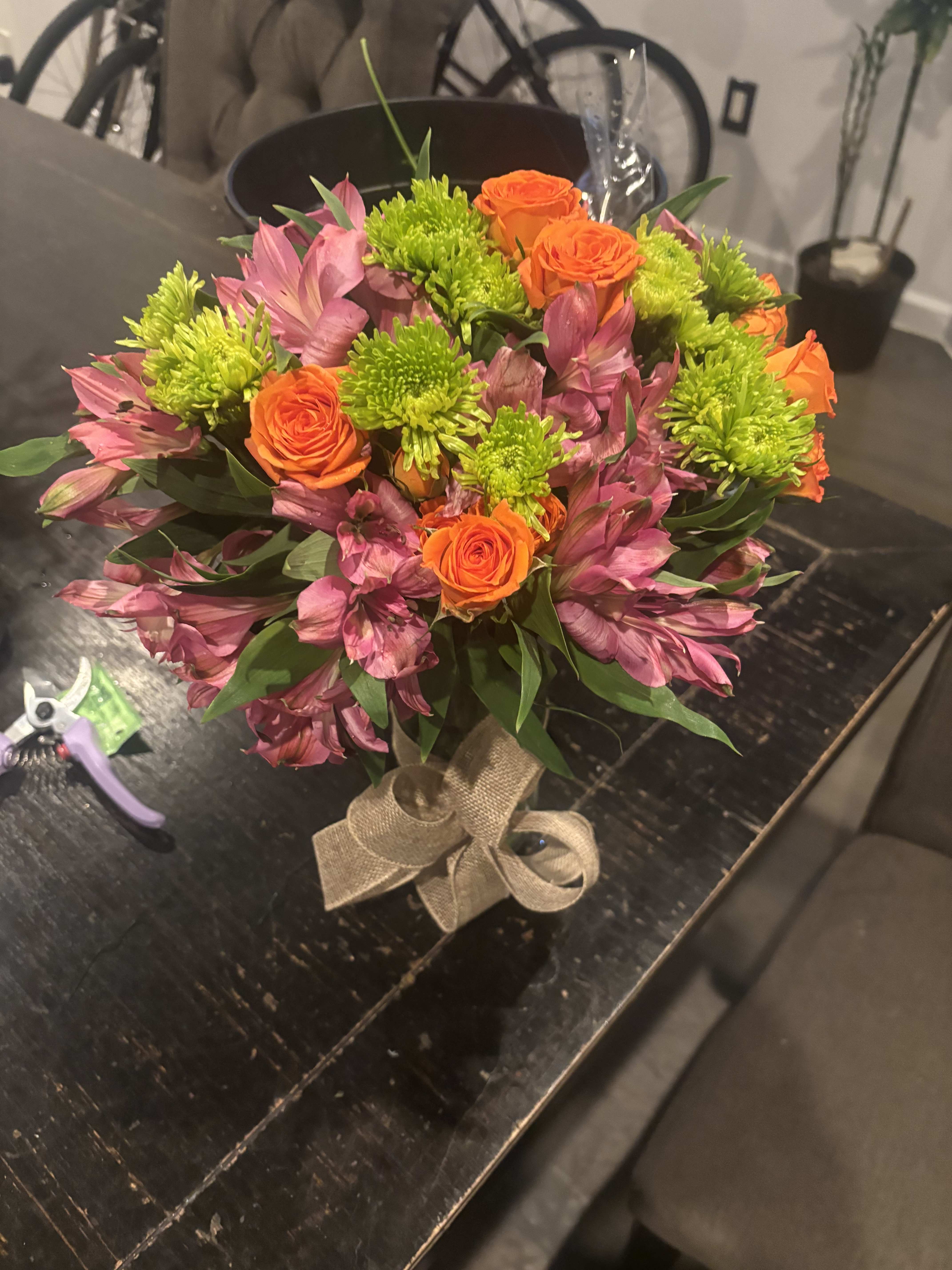 Bouquet of orange roses, pink alstroemeria, and green chrysanthemums tied with burlap ribbon
