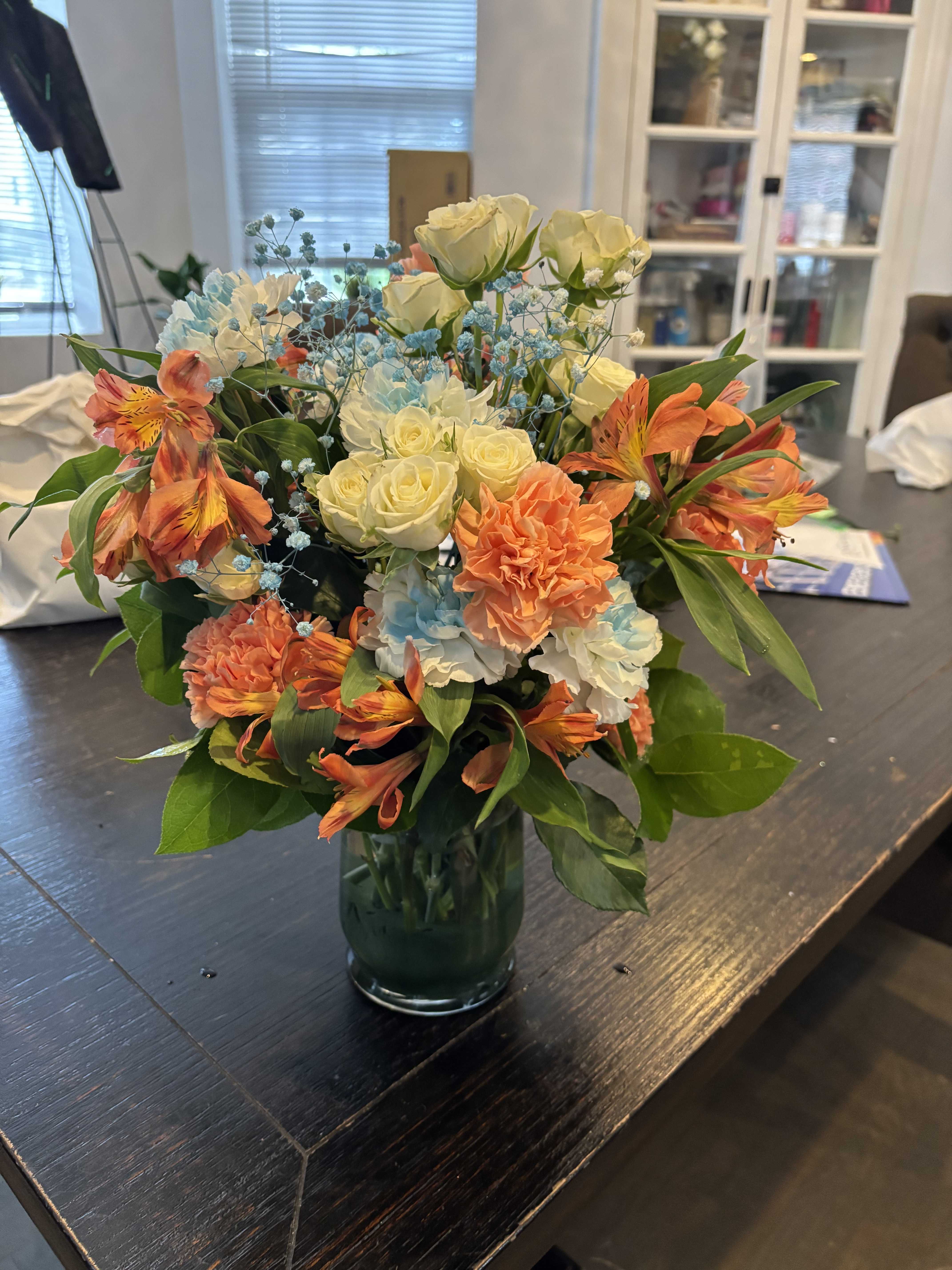 Bouquet of cream roses, orange alstroemeria, and blue filler in a glass vase