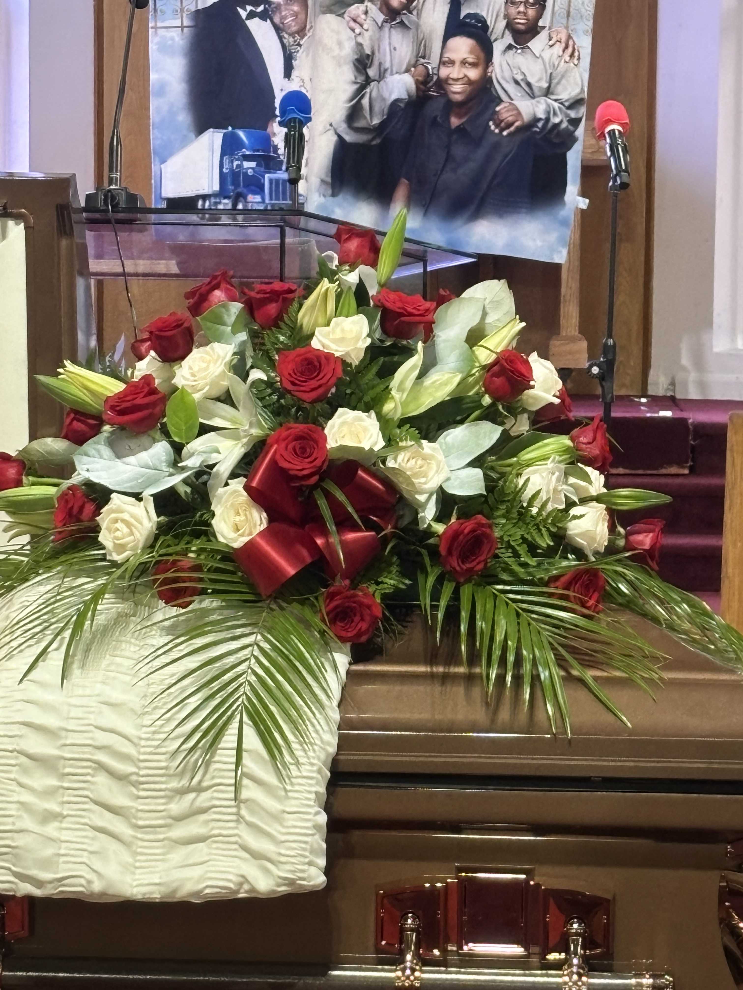 Large red and white rose arrangement on a casket with ribbon and palm fronds