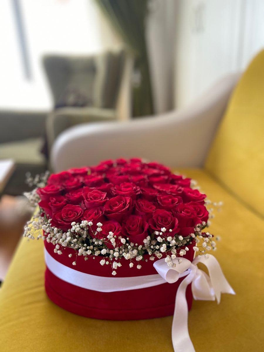 caja con rosas By Special Moment´S - A lush dome of tightly packed red roses set in a round hatbox creates an immediate romantic impact-perfect as a birthday bouquet, anniversary roses gift, or a Valentine's Day surprise for the person you want to make feel adored. The red roses deliver classic, passionate color while a ring of small white filler flowers around the base adds a delicate, sparkling contrast that makes each bloom pop.  Arranged in a red round box and finished with a white satin ribbon tied around the hatbox, this presentation reads like an elegant gift and travels well for delivery. The compact dome shape gives the arrangement a polished, modern silhouette ideal for a bedside table, desk, or dining centerpiece. Order sizing and care details are available at checkout to ensure the roses stay fresh through the moment you plan to share them.
