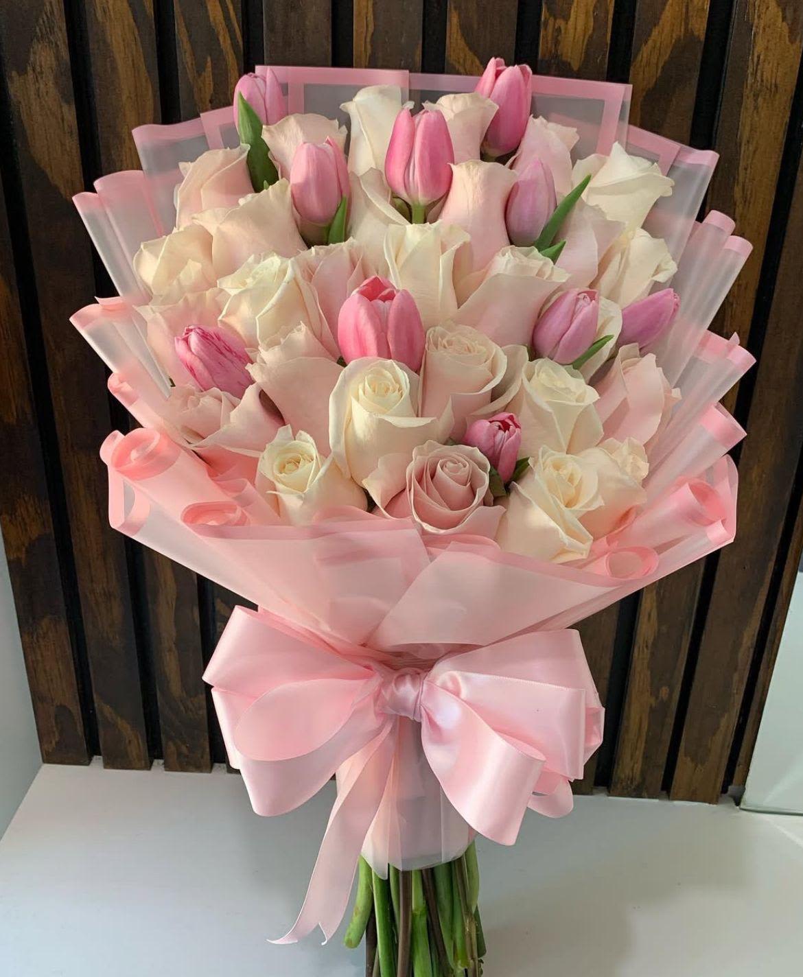 ramo de rosas y tulipanes By Special Moment´S - Pale pink and white roses mingled with fresh pink tulips create a soft, romantic bouquet perfect for an anniversary bouquet or a thoughtful birthday bouquet - the kind that makes the person you're thinking of feel cherished and seen. The combination of dense rose heads and the playful tulip shapes gives a gentle, feminine look ideal for romantic occasions, Mother's Day, or simply saying "I'm thinking of you" with a touch of elegance.  Hand-tied in a full, rounded presentation, the arrangement is wrapped in layered translucent pink tissue and finished with a large pink satin ribbon for a polished, gift-ready finish. The mix of blush and white blooms offers subtle contrast and texture: lush rose petals provide depth while tulips add fresh movement. Order as shown for a medium hand-tied size; to keep the flowers at their best, trim stems, change water daily, and keep the bouquet away from direct heat and drafts.