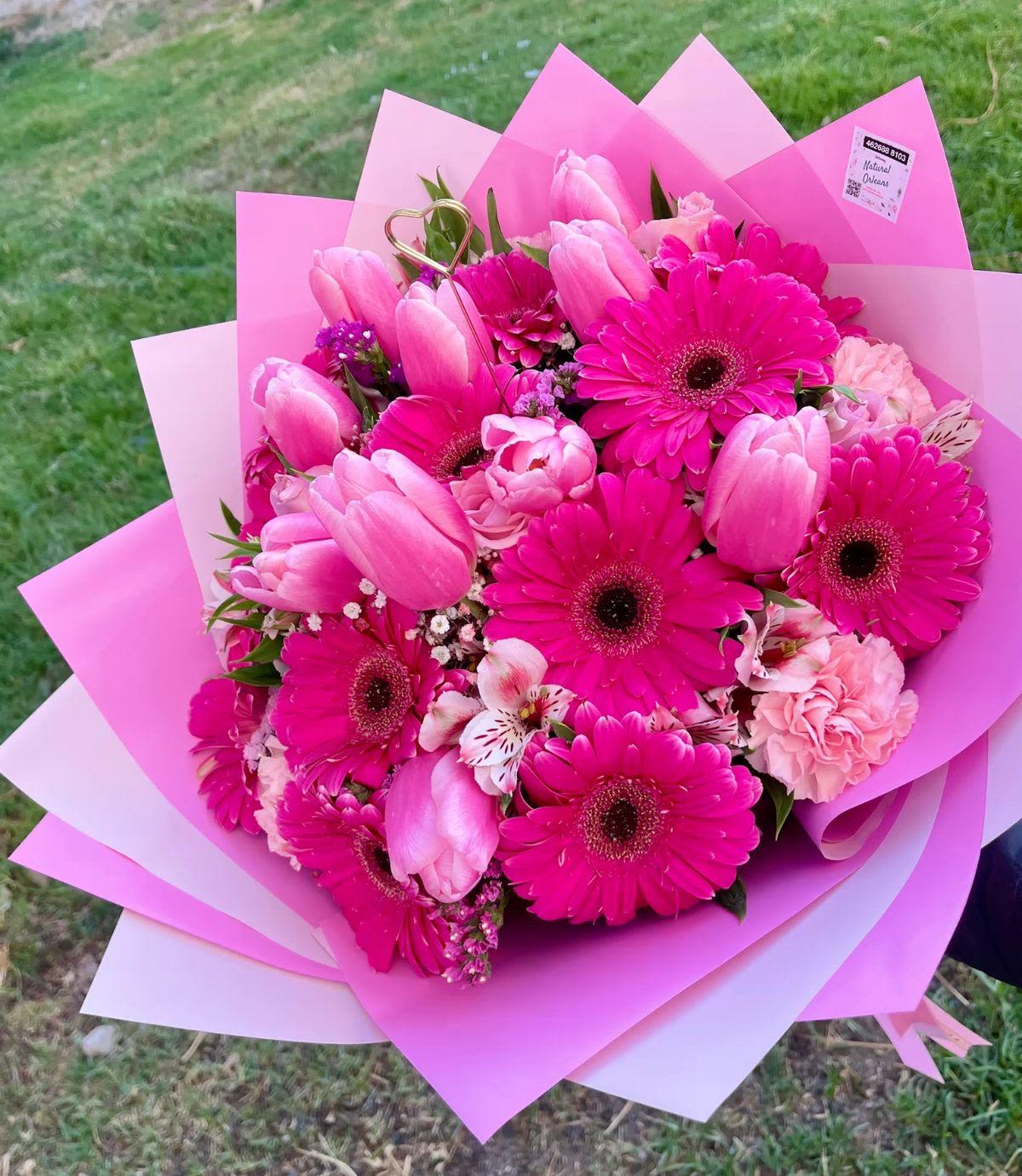 arreglo de gerber y tulipanes By Special Moment´S - Vivid pink gerbera daisies paired with soft pink tulips make a joyful, eye-catching statement in this flower arrangement-perfect as a birthday bouquet, a thank-you gift, or a romantic surprise. The bright, celebratory look is ideal for the person you want to lift up: she'll feel noticed and cheered by the bold pink tones and the fresh, lively mix of shapes.  This arrangement includes pink gerbera daisies, soft pink tulips, pale carnations, and delicate alstroemeria in shades of pink, purple, and white, all wrapped in layered pink wrapping paper and finished with ribbon and a decorative floral pick. The contrast between the rounded daisy faces and the sleek tulip buds creates appealing texture, while the carnations and alstroemeria add fullness and soft accents. The presentation is compact and gift-ready, designed to arrive looking polished and bright.  A versatile choice for everyday gifting or special moments, this bouquet reads as both playful and thoughtful-the kind of gift that makes someone feel truly seen. Care is simple: keep stems in fresh water, trim a little off the ends if needed, and display away from direct heat to extend its vase life.