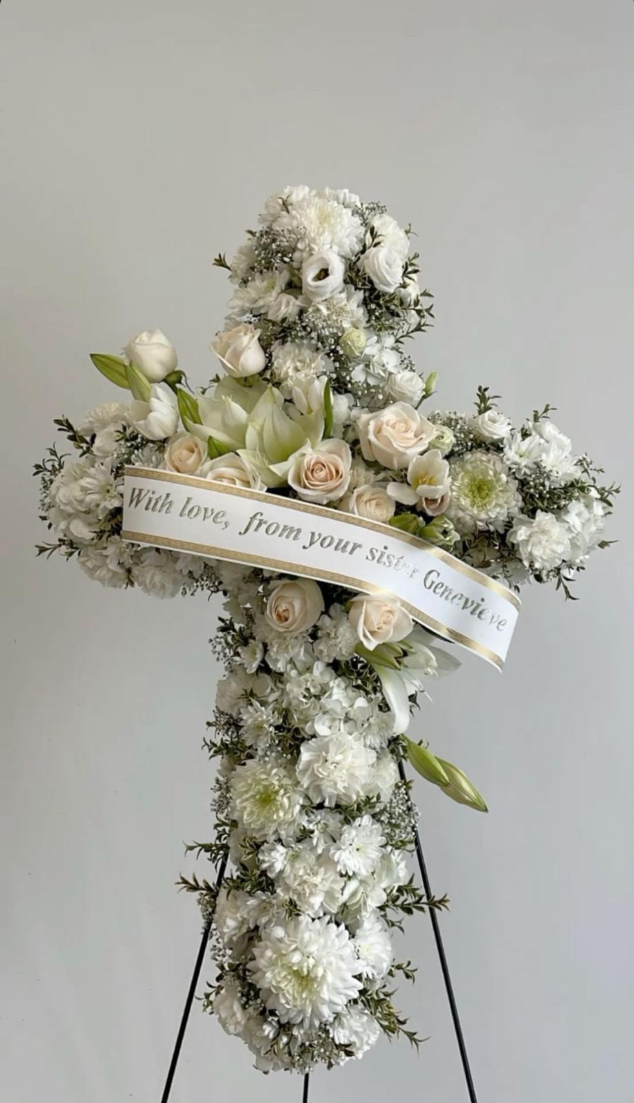 cruz de clavel, rosa y cinta perzonalizada By Special Moment´S - A serene standing sympathy cross designed to honor a loved one with quiet, graceful presence - a funeral flower arrangement that offers comfort and respect. The cross-shaped arrangement and satin ribbon banner make it clear this is a memorial tribute, perfect for a viewing, graveside service, or to send condolences to the family you're thinking of.  The cross is mounted on a floral easel and filled with white roses, lilies, chrysanthemum and daisy-like blooms, with soft peach roses woven through for a gentle, warm contrast against the white and green foliage. A satin ribbon banner across the center can be personalized to carry a name or short message, and the overall composition reads formal and peaceful, designed to convey sympathy with dignity.  Made to stand tall at services or beside a gravesite, this arrangement is intended for those mourning a loss and for families planning a meaningful farewell. If you'd like the ribbon personalized, include the exact wording when you order so the message arrives ready for the service.