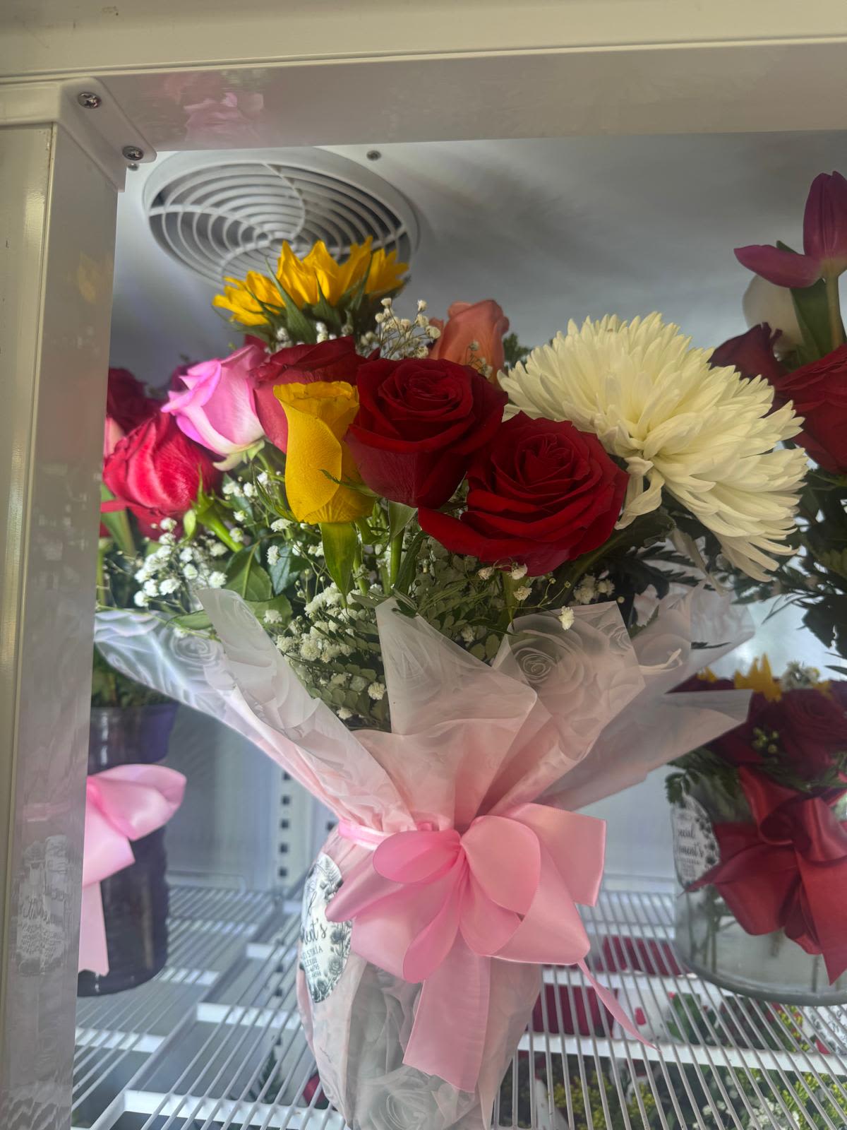 jarron de rosas y girasoles By Special Moment´S - Deep red roses and bright pink blooms mingle with a single sunny yellow calla lily and a large white chrysanthemum to create a bouquet that reads romantic yet fresh - perfect as a birthday bouquet, anniversary roses gift, Valentine's Day arrangement, or a thoughtful thank-you. The combination of red and pink tones gives her a feeling of warmth and affection, while the white chrysanthemum and delicate white filler flowers bring a crisp, elegant contrast so the recipient feels both cherished and truly seen.  This mixed flower arrangement includes roses, chrysanthemums, calla lilies and small white fillers, wrapped in translucent white floral wrap and finished with a wide pink ribbon for a polished, gift-ready presentation. Delivered in a vase, the colors - red, pink, white and yellow - work together to offer visual depth and texture: velvety rose petals, the smooth trumpet of the calla, and the full, cushiony chrysanthemum. Ideal for sending to a partner, close friend, or mentor, it arrives arranged and ready to display; to keep blooms fresh, place in clean water and trim stems every few days.