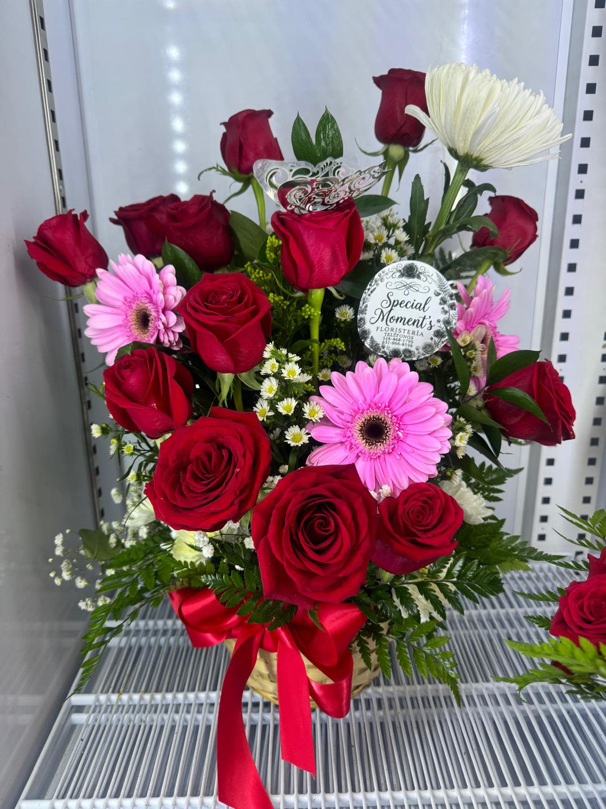 canasta de rosas y gerber By Special Moment´S - A lush cluster of red roses and bright pink gerbera daisies arranged in a rounded basket makes a vivid statement of affection-perfect as a birthday bouquet, anniversary roses alternative, or just because gift to show appreciation. This flower arrangement for romantic occasions and celebrations balances passionate red with playful pink and soft white accents so the person you're thinking of feels adored and celebrated the moment it arrives.  This arrangement combines classic red roses with cheerful pink gerbera daisies and small white daisy-like filler flowers for texture and contrast, all set in a woven basket. A wide red satin ribbon is tied at the base and decorative floral picks and a florist tag complete the polished presentation. The compact, rounded design makes it easy to display on a table or desk and gives a full, abundant look without overwhelming smaller spaces.  Ideal for sending love, congratulations, or warm thanks, this basket is the kind of gift that makes someone feel truly seen. No-fuss care-fresh water in the floral foam and a cool spot away from direct sun-will help the blooms last and brighten their day for as long as possible.