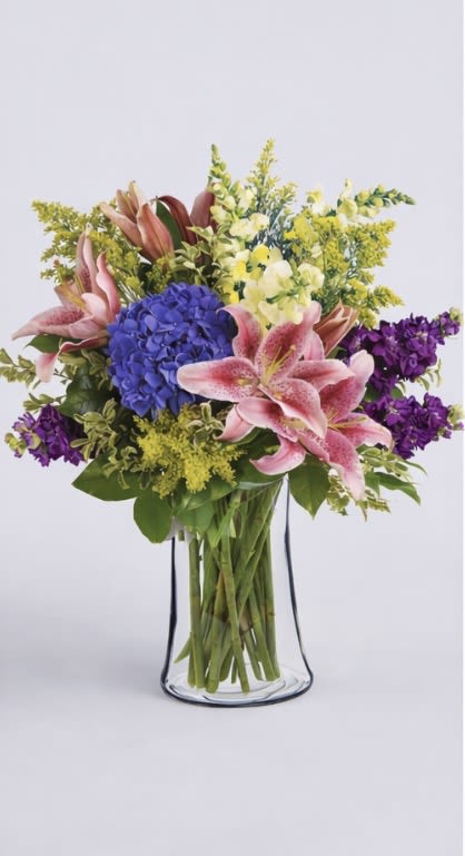 Bouquet of pink lilies, blue hydrangea, and purple flowers in a clear glass vase