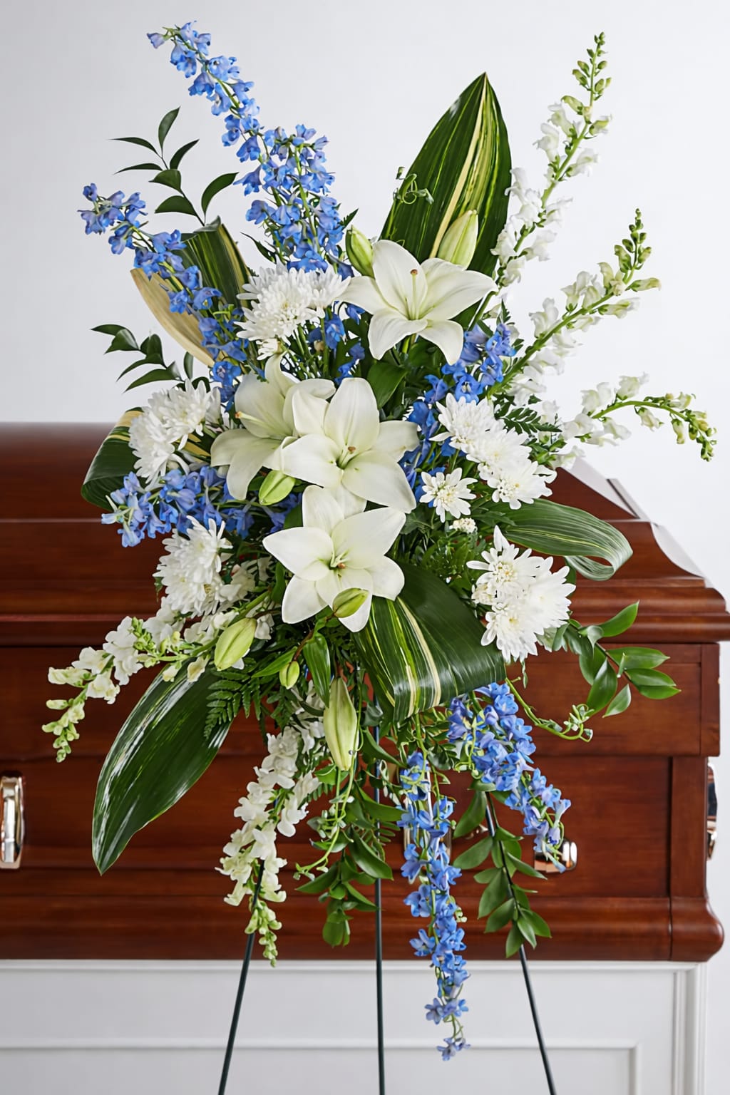White lilies and blue flowers in a standing funeral spray