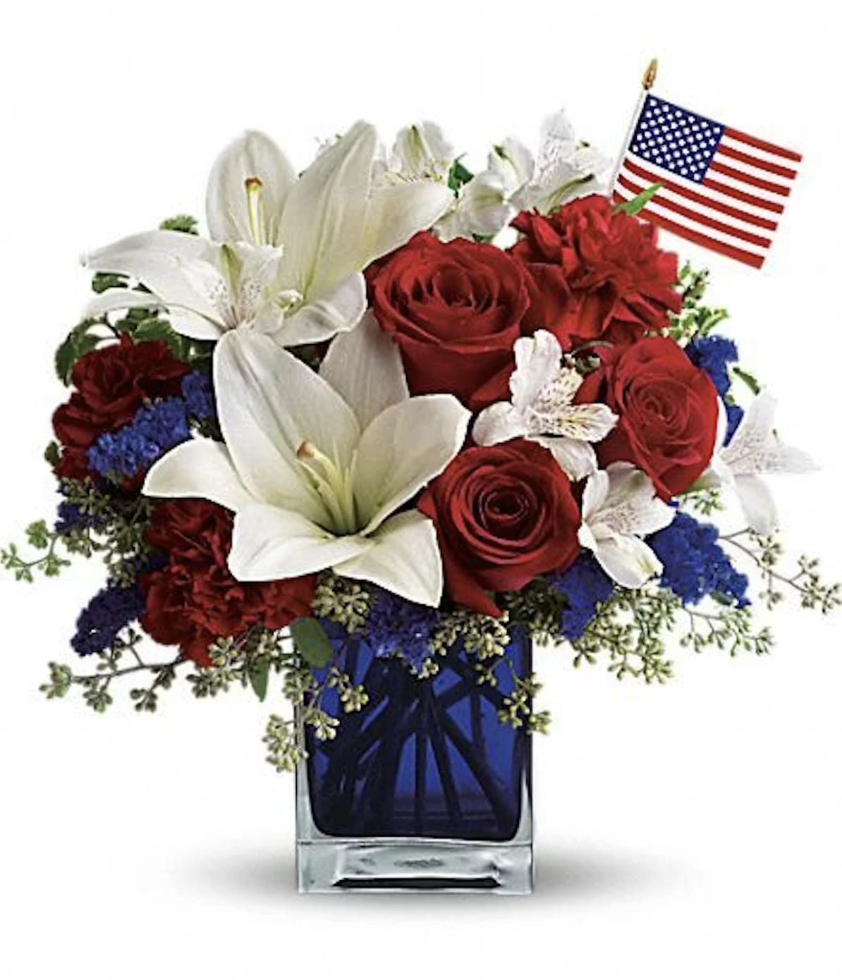 American The Beautiful - A patriotic pick to send a brave veteran, decorate your Fourth of July picnic, or celebrate Memorial Day. Lush red, white and blue flowers are presented in a deep blue glass cube vase along with an American flag. Red roses, white asiatic lilies, white alstroemeria, blue statice and red carnations are gathered with green pitta negra, seeded eucalyptus and a small American flag in a cobalt blue glass cube.